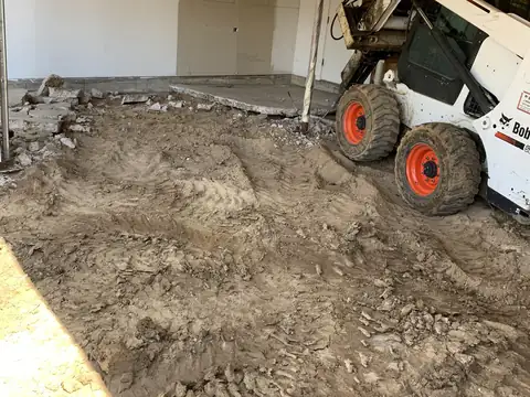 Skid steer loader removing broken concrete and dirt from a garage floor