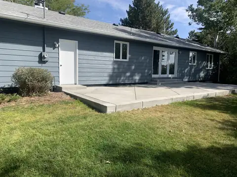 Green lawn in front of a new concrete patio behind a blue ranch house