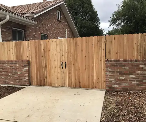 New cedar fence and double gate set between two brick pillars at the end of a concrete driveway