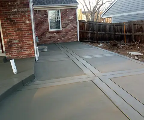Freshly poured scored concrete patio beside a brick house and wood fence